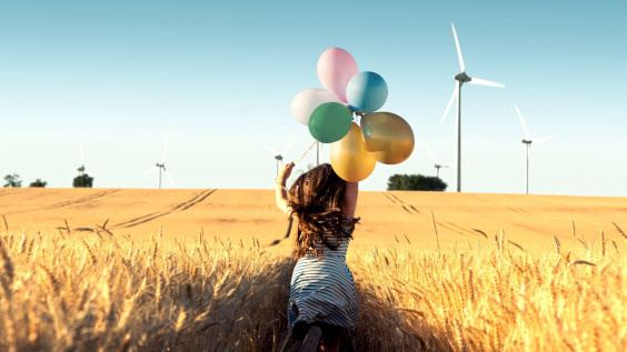 Girl with balloons running through windmill field