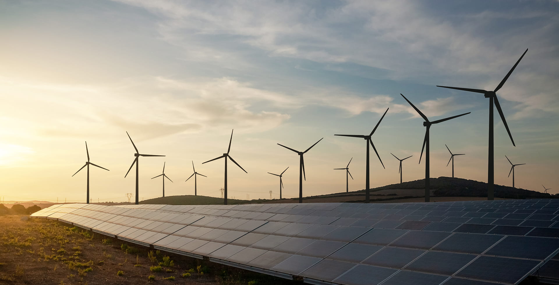 Windturbinen und Solarmodule mit Strommasten im Hintergrund 